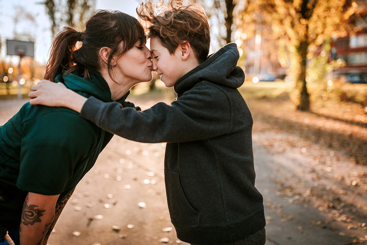 A mom kisses her preteen son on those nose. 